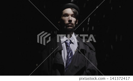 Serious man standing under a dramatic spotlight in the rain Serious man standing under a dramatic spotlight in the rain 141372417