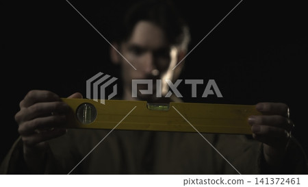 Hands holding a yellow spirit level in dramatic low light Hands holding a yellow spirit level in dramatic low light 141372461