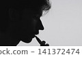 Relaxed side profile silhouette of man smoking cigarette against neutral background with clean natural light, strong contrast, minimal composition, commercial concept, calm atmosphere 141372474