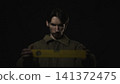 Serious man holding a yellow measuring strip in dark studio 141372475