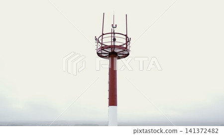 Red and white tower mast against a cloudy sky Red and white tower mast against a cloudy sky 141372482