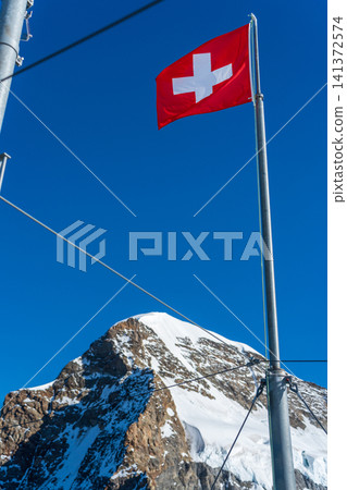 The flag at the Sphinx Observatory and the summit of the Jungfrau mountain. Jungfraujoch, Canton of Bern, Switzerland. 141372574