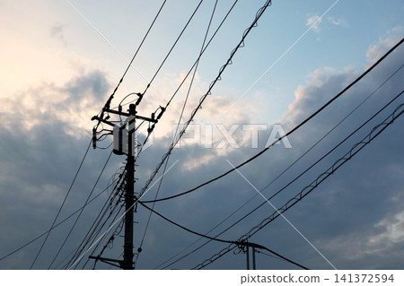暮色中,電線桿和電線的輪廓線勾勒出一片天空;這是居民區的日落景象。 暮色中,電線桿和電線的輪廓線勾勒出一片天空;這是居民區的日落景象。 141372594