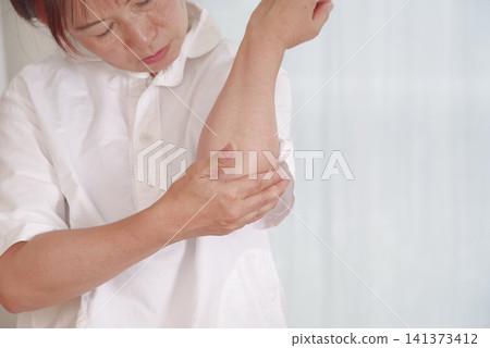 A middle-aged woman suffering from elbow pain touches the affected area. 141373412