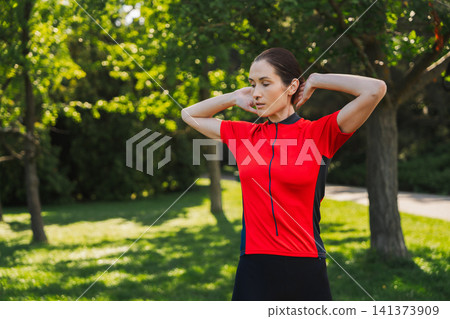 Woman stretches outdoors in a park on a sunny day Woman stretches outdoors in a park on a sunny day 141373909