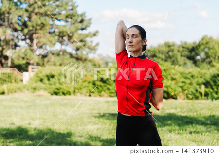 Woman stretches her arm in a park during daylight Woman stretches her arm in a park during daylight 141373910