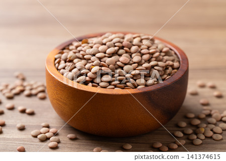 Raw green lentils in a wooden bowl on a wooden background Raw green lentils in a wooden bowl on a wooden background 141374615