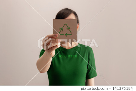 Volunteer woman holding a recycling symbol card in front of her Volunteer woman holding a recycling symbol card in front of her 141375194