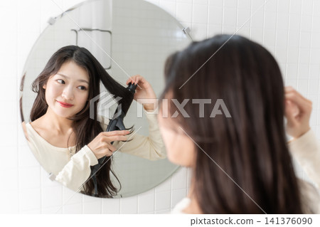 A young woman curls her hair with a curling iron at the bathroom sink. (Beauty image) A young woman curls her hair with a curling iron at the bathroom sink. (Beauty image) 141376090