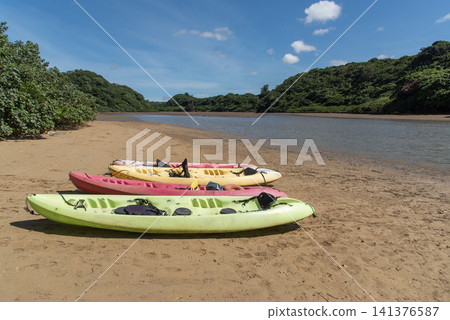 A clear blue sky and a shallow beach surrounded by greenery where the kayak is placed. A clear blue sky and a shallow beach surrounded by greenery where the kayak is placed. 141376587