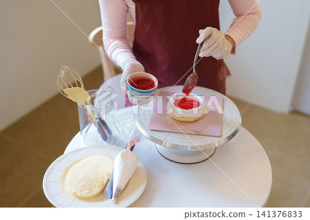Asian woman applying red fruit glaze to homemade cake with spoon in bright modern kitchen with copy space Asian woman applying red fruit glaze to homemade cake with spoon in bright modern kitchen with copy space 141376833