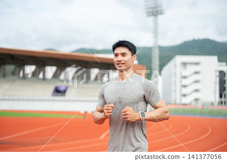 Asian athletic man enjoy running or jogging on racetrack in sports stadium. 141377056