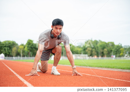 Asian man sprinter focused while crouching in start position ready to run on track in sports stadium Asian man sprinter focused while crouching in start position ready to run on track in sports stadium 141377095