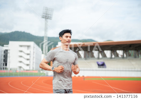 Asian sportsman running fast with a smile on racetrack in sports stadium. Asian sportsman running fast with a smile on racetrack in sports stadium. 141377116