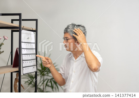 Senior Asian man with dementia struggles to set the time and day on his watch. Senior Asian man with dementia struggles to set the time and day on his watch. 141377414