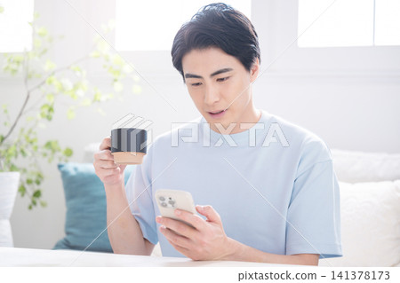 A Japanese man uses his smartphone while drinking coffee and checking information, reflecting his work-from-home lifestyle. A Japanese man uses his smartphone while drinking coffee and checking information, reflecting his work-from-home lifestyle. 141378173