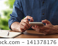 A man is using a smartphone app at a table. He taps the phone screen. 141378176