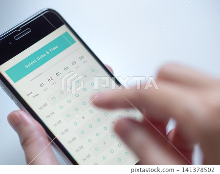 A photo of a woman's hands operating her smartphone to make an online reservation (screen image is original). A photo of a woman's hands operating her smartphone to make an online reservation (screen image is original). 141378502