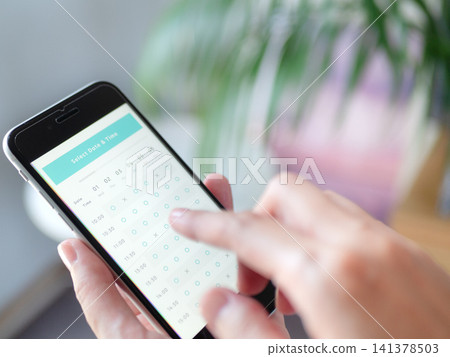 A photo of a woman's hands as she makes an online reservation using her smartphone (screen image is original). A photo of a woman's hands as she makes an online reservation using her smartphone (screen image is original). 141378503