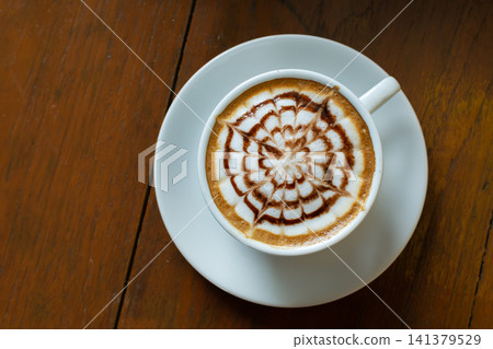 Top view of cappuccino intricate latte art served white cup wooden table creating warm cafe atmosphere for coffee lovers relaxation Top view of cappuccino intricate latte art served white cup wooden table creating warm cafe atmosphere for coffee lovers relaxation 141379529