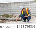 Engineer inspecting concrete surface at construction site while using tablet safety equipment for quality control structural assessment project supervision 141379534