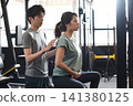 A young Asian woman receives posture instruction from an Asian male trainer at a personal gym. 141380125