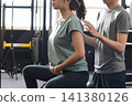 A young Asian woman receives posture instruction from an Asian male trainer at a personal gym. 141380126