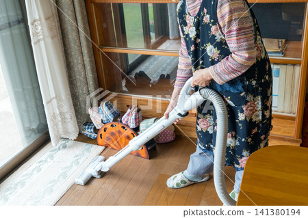 An elderly woman vacuuming her home An elderly woman vacuuming her home 141380194