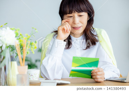 A middle-aged woman looking at her savings passbook in the living room A middle-aged woman looking at her savings passbook in the living room 141380493