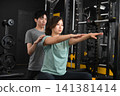 A young Asian woman being instructed by a young male trainer at a personal gym. 141381414