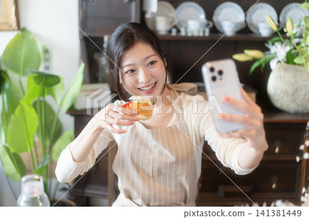 A young woman smiles and takes a selfie at a guesthouse with a traditional Japanese house design. A young woman smiles and takes a selfie at a guesthouse with a traditional Japanese house design. 141381449