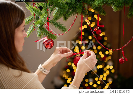 Woman decorating room for Christmas, hanging ornaments on pine garland at home. Woman decorating room for Christmas, hanging ornaments on pine garland at home. 141381675