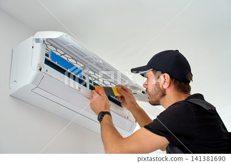 Technician replacing air conditioner filter during home maintenance Technician replacing air conditioner filter during home maintenance 141381690