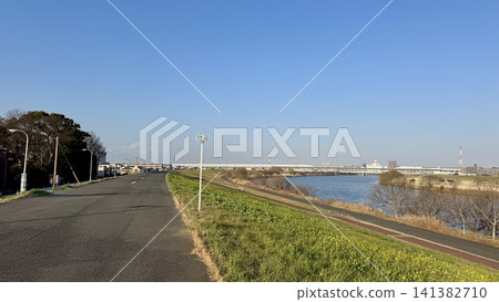 Long paved path beside a broad urban river 141382710