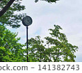 A pole clock standing in a lush green park, against the early summer sky. 141382743