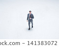 Miniature businessman figure walks on plain white background. 141383072