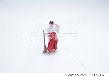Miniature Shinto shrine maiden holds a sweeping broom. 141383073