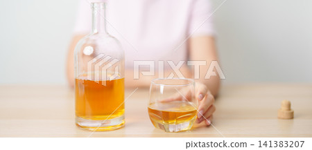woman with glass of whiskey on table, suffering from alcohol addiction and alcoholism concept. depicting emotional distress, depression, substance abuse problem, unhealthy lifestyle and mental health 141383207