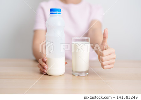 Healthy woman with glass of fresh milk and show thumbs up at home, female drinking for calcium and strong bones, high protein, dairy product for healthy lifestyle, wellness and daily routine concept Healthy woman with glass of fresh milk and show thumbs up at home, female drinking for calcium and strong bones, high protein, dairy product for healthy lifestyle, wellness and daily routine concept 141383249