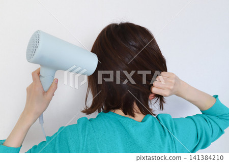 Rear view of a woman drying her hair with a hair dryer Rear view of a woman drying her hair with a hair dryer 141384210