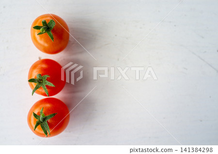 Three ripe tomatoes with fresh green stems arranged vertically on pale white surface, overhead view, clean minimalist food composition with bright natural light and copy space Three ripe tomatoes with fresh green stems arranged vertically on pale white surface, overhead view, clean minimalist food composition with bright natural light and copy space 141384298