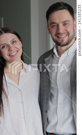 Vertical video Happy married couple owners of a new apartment show the key looking at camera. Wife and husband hug and smile in living room in apartment. Vertical video Happy married couple owners of a new apartment show the key looking at camera. Wife and husband hug and smile in living room in apartment. 141385235