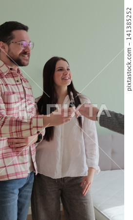 Vertical video Real estate agent is giving keys to buyers of new apartment. Happy husband and wife are hugging, man is shaking hands with man realtor. Vertical video Real estate agent is giving keys to buyers of new apartment. Happy husband and wife are hugging, man is shaking hands with man realtor. 141385252