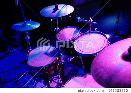 Drum set on stage bathed in vibrant blue and purple light Drum set on stage bathed in vibrant blue and purple light 141385310