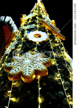 Gingerbread and snowflake ornaments on glowing Christmas tree at night Gingerbread and snowflake ornaments on glowing Christmas tree at night 141385330