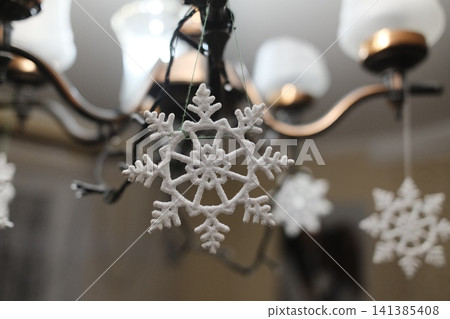 White frosted snowflake ornament adorns a metal chandelier in a living room for holiday cheer 141385408