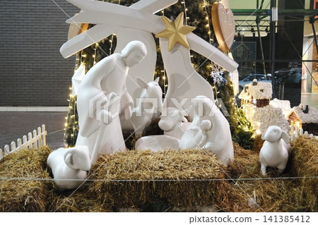 Holiday nativity display featuring white figures of the Holy Family and animals in a bright commercial space, lit up for Christmas Holiday nativity display featuring white figures of the Holy Family and animals in a bright commercial space, lit up for Christmas 141385412