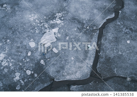 Close up view of a frozen surface featuring icy cracks and broken pieces of ice 141385538