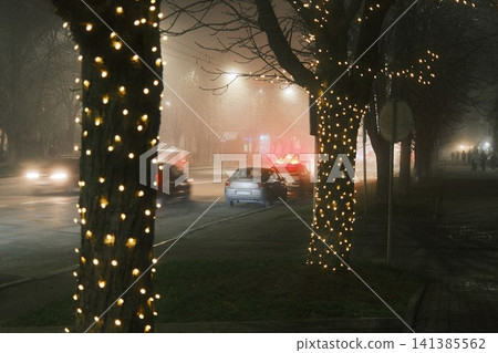 Foggy night street with illuminated trees and a car on fire Foggy night street with illuminated trees and a car on fire 141385562