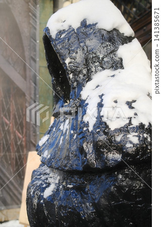 Snow-covered black abstract sculpture of a hooded figure side view Snow-covered black abstract sculpture of a hooded figure side view 141385671